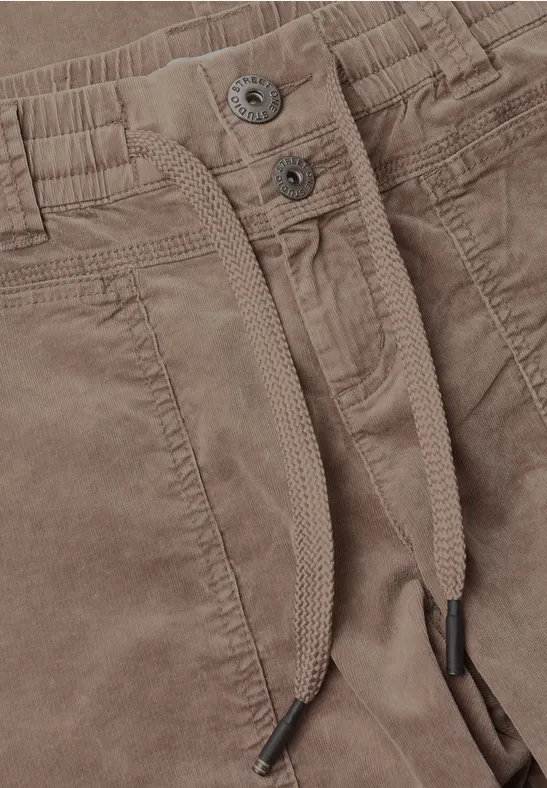 Nahaufnahme einer braunen Cordhose mit Bündchen, Kordelzug, Taschen und Metallknöpfen.