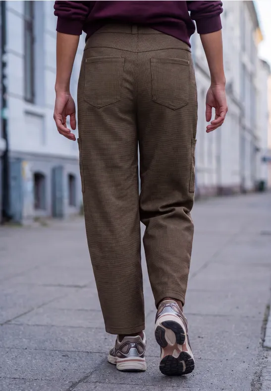 Person in brauner Hose und weißen Sneakern geht auf einem Fußgängerweg an Häusern vorbei.