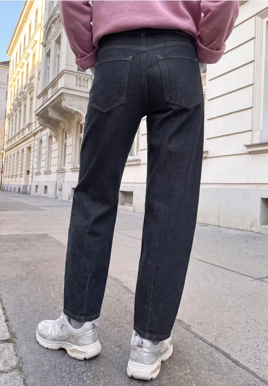 Person in dunklen Jeans und weißen Sneakers geht auf einem Gehweg vor historischen Häusern.