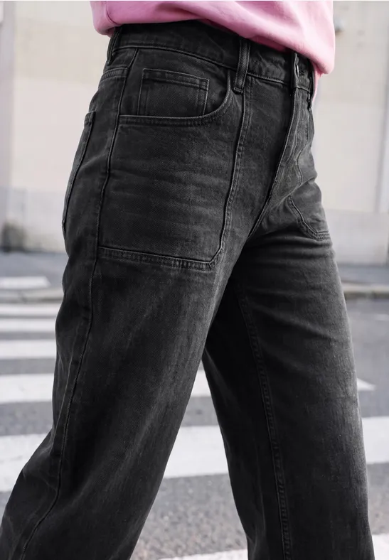 Nahaufnahme einer Person in weiten schwarzen Jeans und rosa Oberteil beim Überqueren einer Straße.
