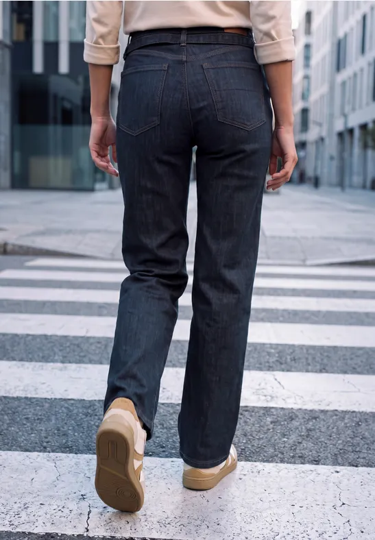 Vue de dos d'une personne en jean et baskets beiges traversant un passage piéton en ville.