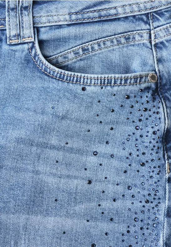 Close-up van een lichtblauwe spijkerbroek met voorzak en kleine metalen studs als versiering.