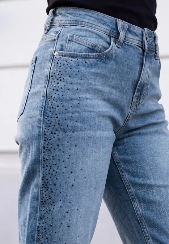 Close-up van een lichtblauwe high-waist jeans met glinsterende studs op het bovenbeen.