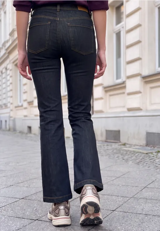 Persoon in donkere wijde jeans en sneakers loopt op een stoep langs een klassieke gevel.