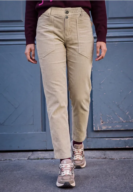 Person trägt beige Cordhose mit Seitentaschen, kombiniert mit Sneakers und weinrotem Oberteil.