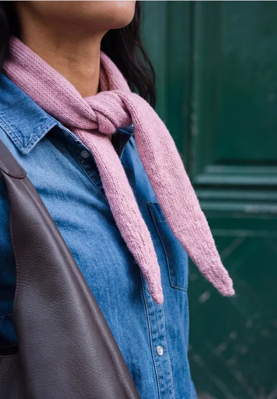 Vrouw in jeansoverhemd met roze sjaal en bruine tas voor een groene achtergrond