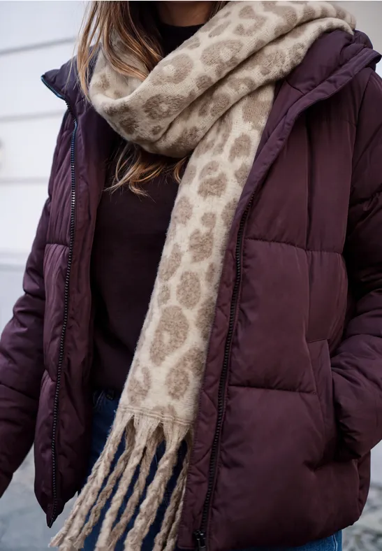 Eine Person trägt eine violette Daunenjacke und einen beigen Schal mit Leomuster.