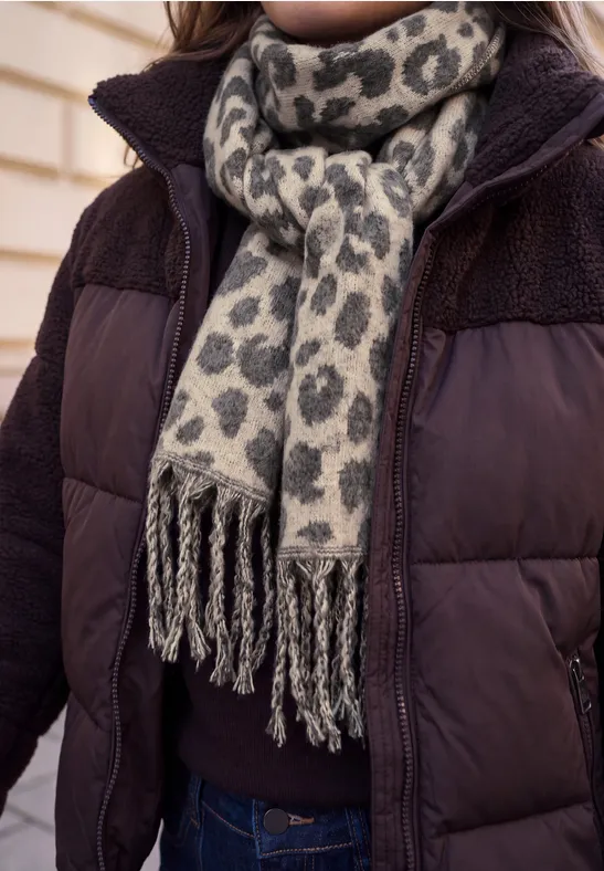 Person im Daunenmantel mit grauem, schwarz gemustertem, fransigem Schal im Leopardenprint.