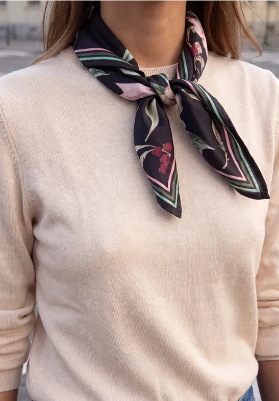 Vrouw draagt beige trui en zwarte zijden sjaal met roze print om haar hals geknoopt.