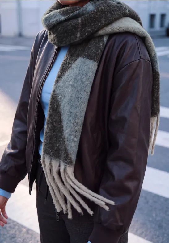 Personne porte une veste en cuir marron foncé et une large écharpe bicolore en laine dans la rue.