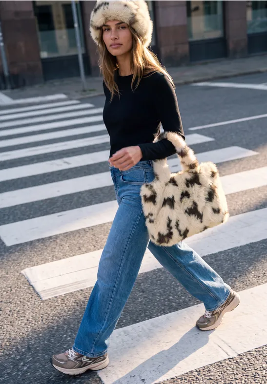Frau mit Pelzmütze, schwarzem Pullover, blauen Jeans und flauschiger Tasche über Zebrastreifen.
