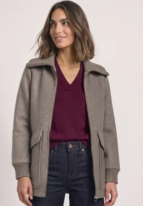 Frau in braunem Mantel, bordeauxrotem V-Ausschnitt-Pullover und Jeans