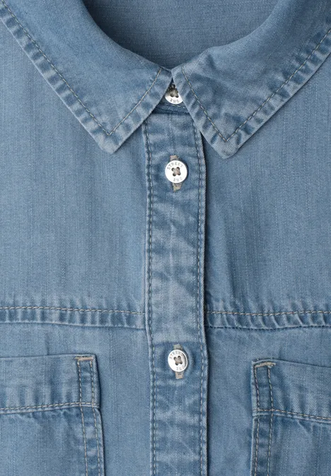 Nahaufnahme einer blauen Jeansjacke mit Metallknöpfen und aufgesetzten Brusttaschen.