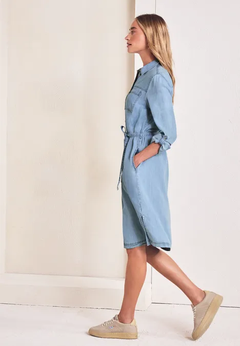 Seitliches Profil einer Frau in hellblauer Denim-Overall mit Gürtel und Plateau-Schuhen.