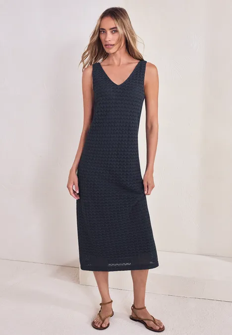 Femme en robe midi sans manches à encolure V, motif à petits carreaux, avec sandales plates.