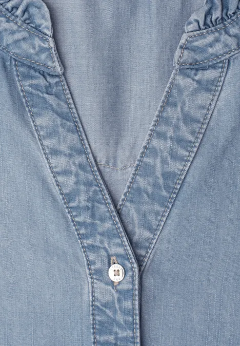 Close-up van een lichtblauw denim bovenstuk met V-hals en knoop