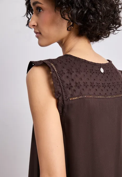 Frau im Profil trägt ein ärmelloses, braunes Top mit Spitzenbesatz auf den Schultern.