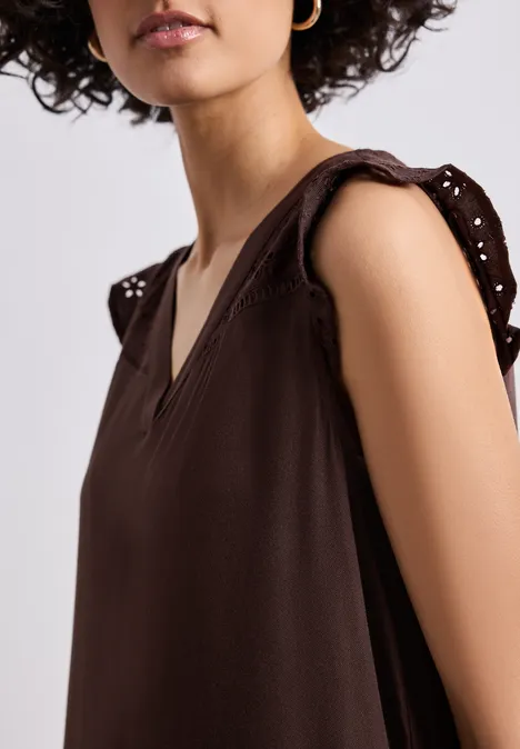 Frau in braunem, ärmellosem V-Ausschnitt-Oberteil mit dekorativen Lochstick-Ärmeln.