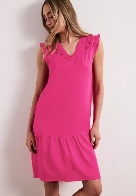 Frau in knielangem pinkfarbenen ärmellosem Kleid mit Spitzenbesatz auf weißem Hintergrund