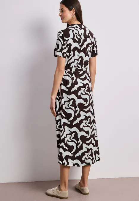 Frau in midilangem, schwarz-weiß gemustertem Kleid, seitlich stehend.