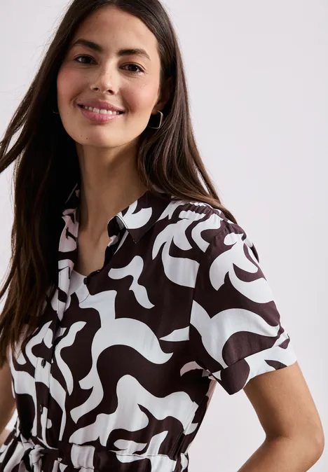 Frau trägt kurzärmelige Bluse mit schwarz-weißem abstraktem Muster vor weißem Hintergrund