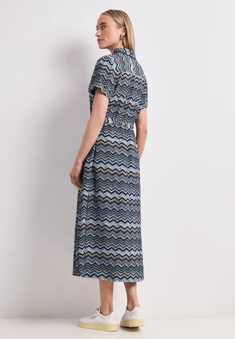 Midi-jurk met zigzagpatroon frozen wave Vrouw in midijurk met blauw-wit-zwart zigzagpatroon, zijaanzicht tegen witte achtergrond.