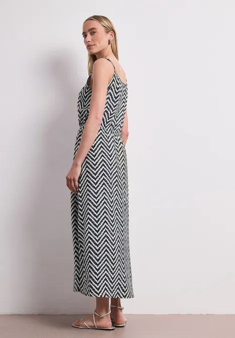 Seitenansicht einer Frau in einem schwarz-weißen Zickzack-Maxi-Kleid mit Spaghettiträgern vor weißem Hintergrund.