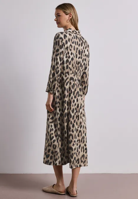 Vrouw in midi-jurk met luipaardprint en driekwartmouwen, zijwaarts staand voor neutrale achtergrond