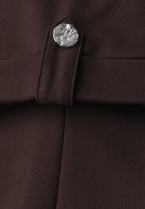 Detailaufnahme eines dunkelbraunen Kleidungsstücks mit silberner, münzförmiger Knopfverzierung und Riegel.