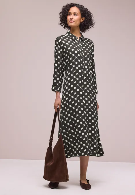 Frau in Midi-Hemdkleid mit weißem Sternmuster, brauner Wildleder-Tasche und braunen Mules.