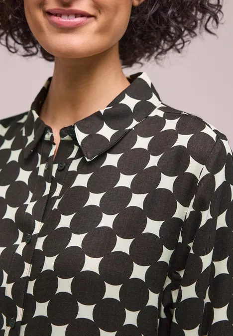 Eine Frau trägt eine schwarz-weiße Bluse mit geometrischem Kreis-Muster und Kragen.