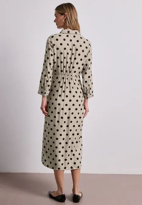 Femme vue de dos portant une robe midi beige à pois noirs, manches 3/4 et chaussures plates