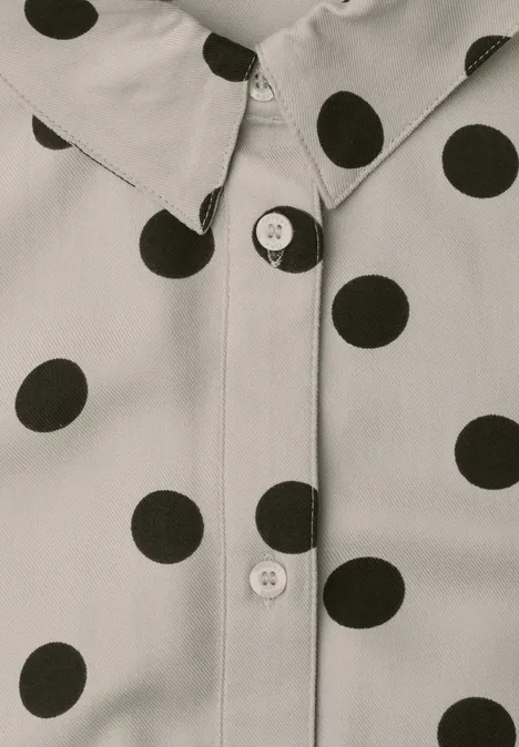Gros plan d’une chemise crème à pois noirs avec boutons visibles.