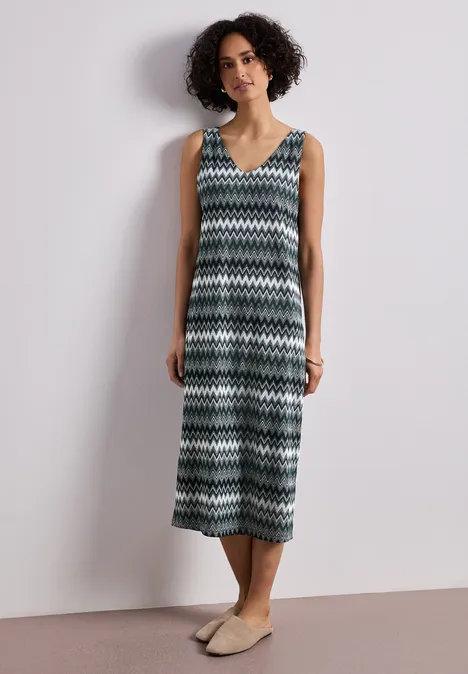 Eine Person trägt ein ärmelloses Midikleid mit Zickzackmuster und flachen Espadrilles.