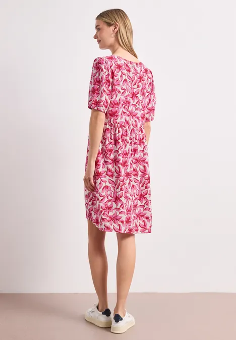 Une femme de profil porte une robe mi-longue rouge à motifs blancs et des baskets.