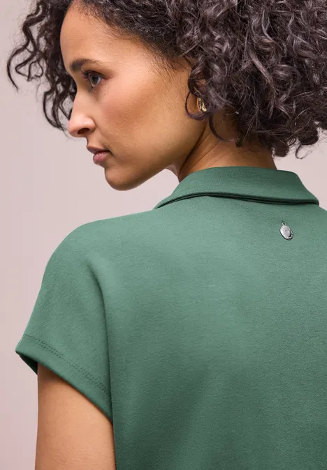 Rückansicht einer Person mit lockigem Haar, die ein grünes Polohemd trägt.