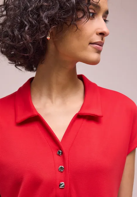 Eine Person mit lockigem Haar trägt ein rotes Poloshirt.