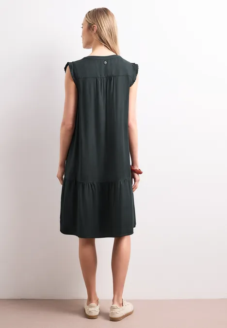 Femme de dos portant une robe noire courte à manches courtes et volants.