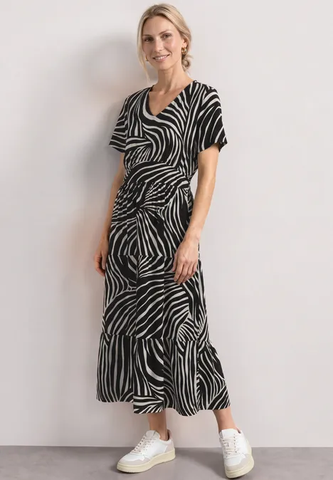 Vrouw in zwart-witte zebrajurk en witte sneakers tegen een lichte achtergrond.