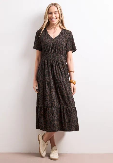 Vrouw in een zwarte midi-jurk met V-hals en luipaardprint, korte mouwen, gecombineerd met witte sneakers.