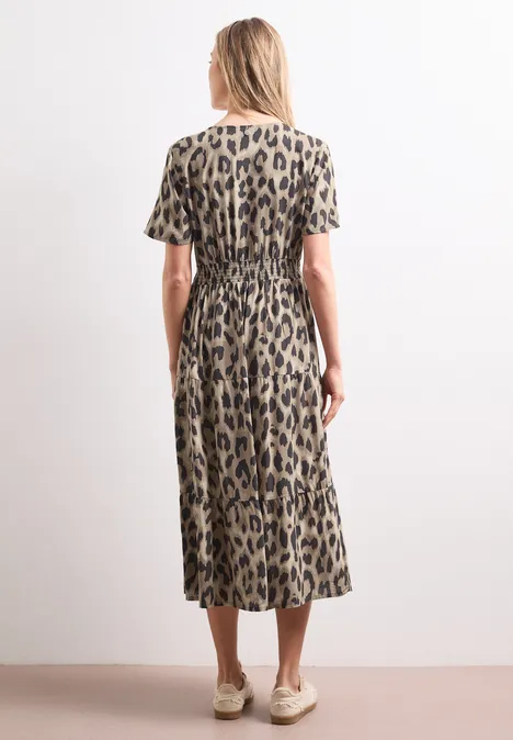 Midi-Kleid mit Print und Smok-Detail timeless beige Rückansicht einer Frau in Midi-Kleid mit Leopardenmuster, kurzen Ärmeln und beigen Schuhen vor weißer Wand.