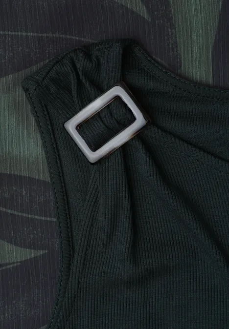 Close-up van een donkergroene stoffen band met een zilverkleurige rechthoekige gesp op camouflageachtergrond.