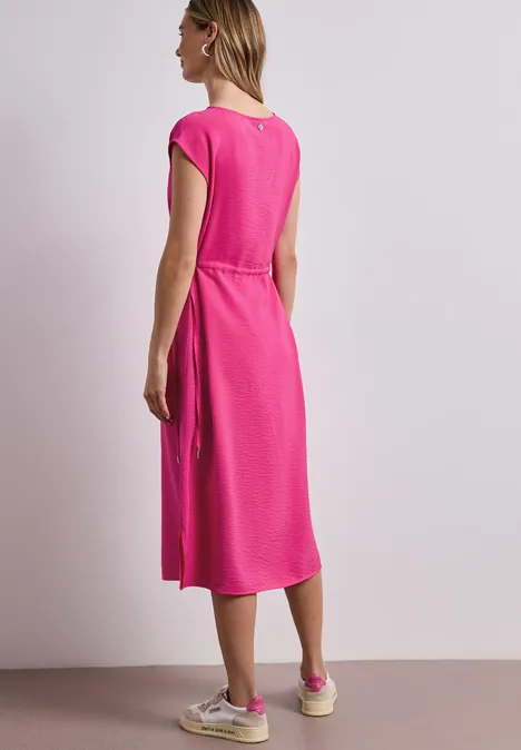 Kobieta tyłem w różowej sukience midi z krótkimi rękawami i białych trampkach.