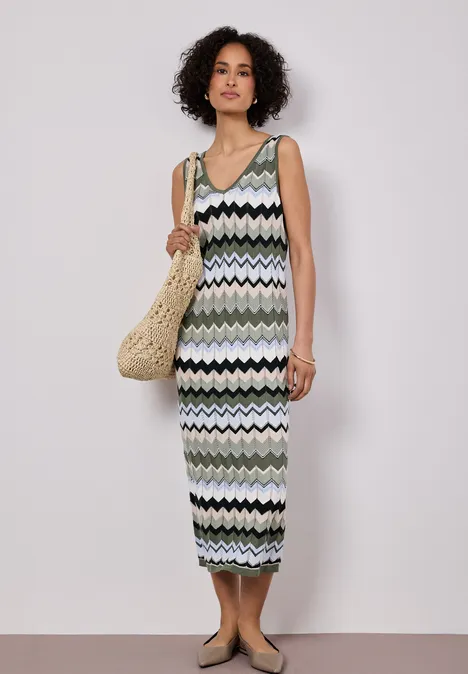 Frau trägt midilanges, ärmelloses, gestricktes Zigzag-Kleid und Korbtasche im sommerlichen Look.