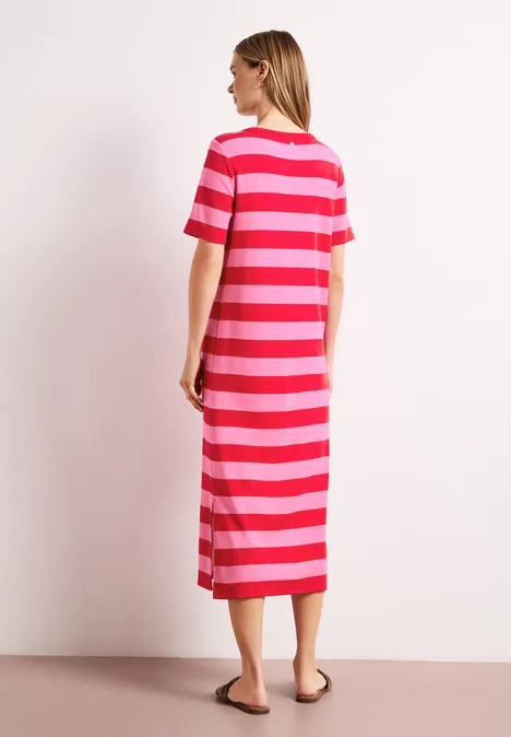 Een vrouw staat zijwaarts in een midi-jurk met rode en roze strepen.