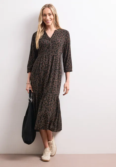 Midi-Kleid mit Split Neck und Print molten earth Frau in midi-langen, braun-schwarz gemustertem Kleid mit 3/4-Ärmeln, hellen Sneakern und schwarzer Tasche.