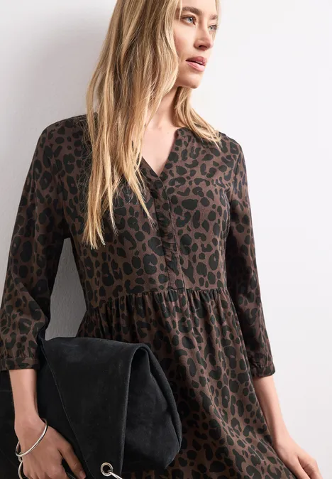 Midi-Kleid mit Split Neck und Print molten earth Frau in braunem Leo-Kleid, 3/4-Ärmel, hält schwarzen Wildleder-Clutch, langes blondes Haar.