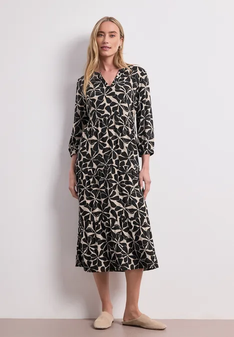 Midi-Kleid mit Split Neck im Ethno-Look Black Frau im schwarzen Midi-Kleid mit beigem Sternmuster, tailliertem Schnitt und beigen Slippern.