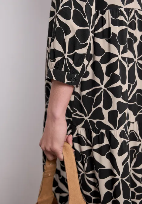 Midi-Kleid mit Split Neck im Ethno-Look Black Person in schwarz-weiß gemustertem Kleid hält eine braune Handtasche.