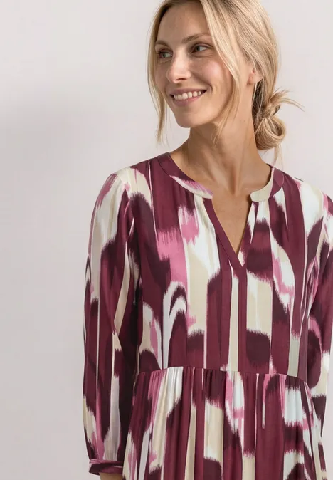 Vrouw in losse jurk met abstracte penseelstreekprint in paars en wit.